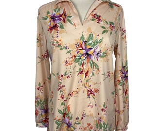 Puede incluir: Una blusa de manga larga con cuello en V y estampado floral. La blusa es de color melocotón con un patrón de flores moradas, naranjas y verdes.