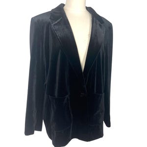 May include: A black velvet blazer with a notched lapel, long sleeves, and two front pockets. The blazer is buttoned and displayed on a mannequin against a white background. The fabric has a soft, luxurious appearance.