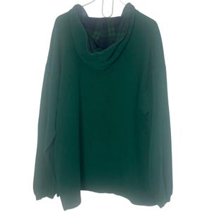 May include: A long-sleeve pullover hoodie in a solid dark green color. The garment features a hood lined with a dark blue and green plaid pattern. The hoodie is displayed on a white hanger against a plain white background, showing the back view.