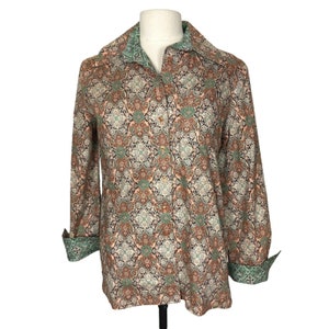 May include: A long-sleeved button-down shirt with a paisley print in shades of brown, green, and white. The shirt has a collar and a button-up front.