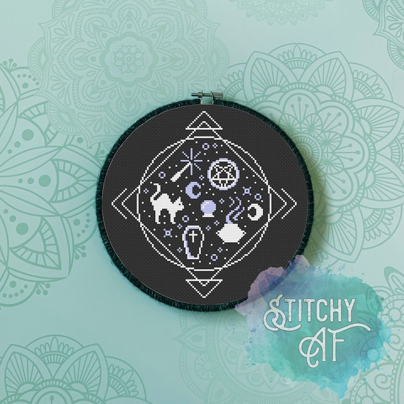 May include: A black and white cross-stitch pattern on a black fabric hoop. The pattern features a cat, a cauldron, a crescent moon, a crystal ball, a coffin, and a star. The pattern is surrounded by a geometric design.