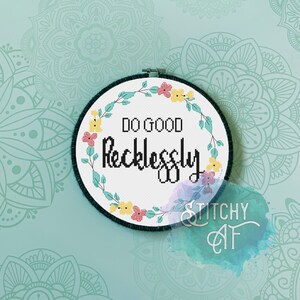 Op de afbeelding: Een witte borduurring met een bloemenkrans en de tekst "Do Good Recklessly" in zwart. De ring is op een lichtblauwe achtergrond met een mandala-patroon.