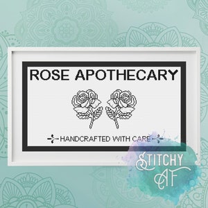 May include: Black and white cross stitch pattern with the text "ROSE APOTHECARY" and two roses. The text "...HANDCRAFTED WITH CARE..." is below the roses.