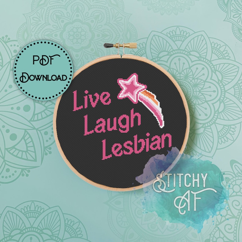 May include: A black embroidery hoop with the text "Live Laugh Lesbian" in pink lettering. A pink star with a rainbow shooting star is above the text. The hoop is on a teal background with mandala designs.