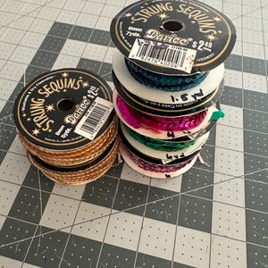 May include: A stack of spools of colorful strung sequins. The spools are labeled "Darice" and "Strung Sequins".