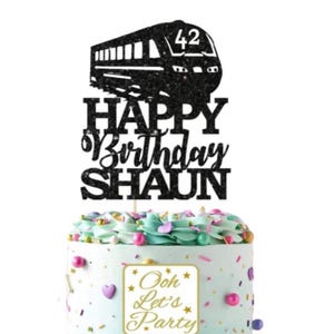 May include: A black glitter cake topper featuring a train silhouette and the number 42. The topper says "HAPPY Birthday SHAUN". The cake is decorated with pastel frosting, sprinkles, and a sign that reads "Ooh Let's Party".