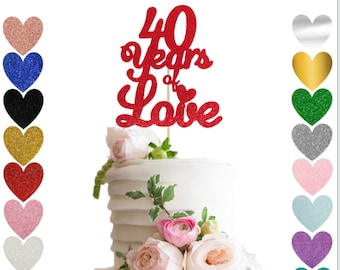 May include: Red glitter cake topper with the text "40 years of love" and a small heart. The topper is on a white cake with pink flowers and the text "Ooh Let's Party".