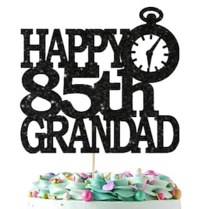 May include: Black glitter cake topper with the text "Happy 85th Grandad" and a clock. The cake topper is on a cake with a white square topper that says "Ooh Let's Party" in gold glitter.