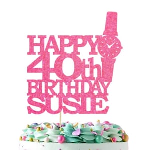 May include: Pink glitter cake topper with the text "Happy 40th Birthday Susie" and a pink glitter watch. A cake with blue and white frosting and sprinkles is in the background. A white square with gold glitter text "Ooh Let's Party" is on the cake.