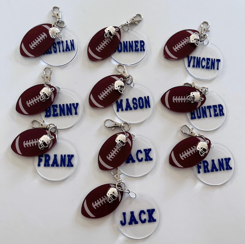 May include: Nine white round acrylic keychains with a maroon football charm attached. Each keychain has a name printed in blue letters: Christian, Conner, Vincent, Benny, Mason, Hunter, Frank, Jack, and Jack.