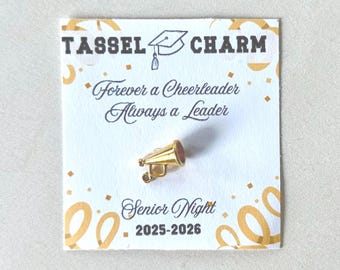 May include: A gold megaphone charm pin with a red interior, displayed on a white card. The card has the text "Tassel Charm," a graduation cap illustration, and the phrases "Forever a Cheerleader Always a Leader" and "Senior Night 2025-2026."