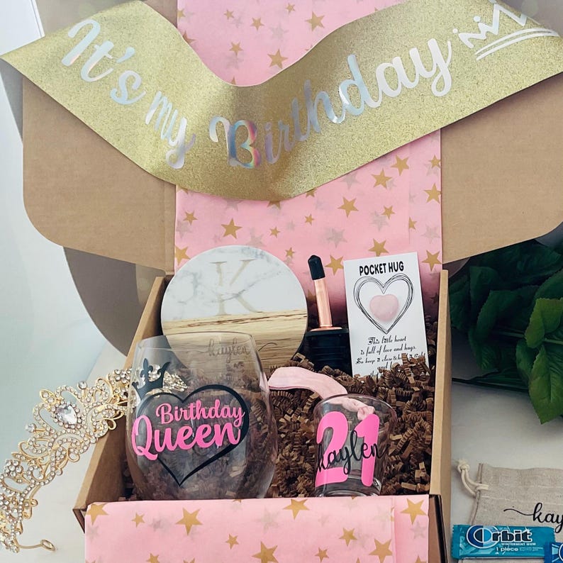 Pode incluir: Uma caixa de presente de anivers&aacute;rio com uma faixa dourada com glitter que diz "It's my Birthday". A caixa cont&eacute;m uma ta&ccedil;a de vinho com o texto "Birthday Queen", um copo de shot, uma tiara e um cart&atilde;o "Pocket Hug".