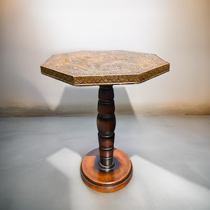 May include: An octagonal side table with a detailed, patterned top. The table has a dark brown, turned pedestal base and a round base. The table's top is approximately 24 inches in diameter.