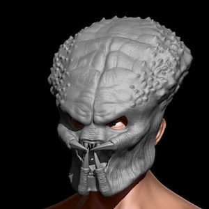 May include: A grey Predator mask with visible teeth and red eyes. The mask has a detailed, alien-like design with a bumpy texture on the forehead and sides. The mask is set against a black background.
