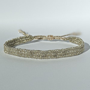 May include: A silver and beige braided bracelet with a simple knot closure.