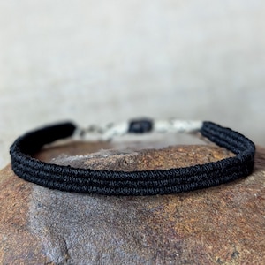 Op de afbeelding: Een zwarte gevlochten koord armband met een zilveren sluiting.