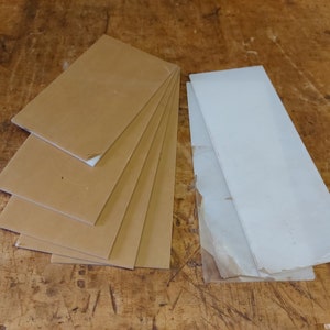 Könnte beinhalten: Ein Stapel aus sechs braunen rechteckigen Blättern aus Acrylkunststoff und ein einzelnes weißes rechteckiges Blatt aus Acrylkunststoff.