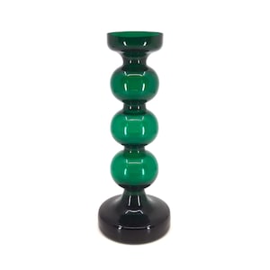 May include: A decorative glass candlestick holder. The candlestick features a dark green top and three spherical green accents stacked on a black base. The design is a modern take on a classic candle holder.