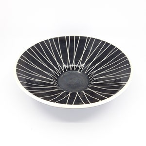 Può includere: Una ciotola in ceramica nera con un design geometrico bianco. Il design presenta linee radianti che creano un motivo a raggiera.