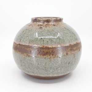 Op de afbeelding: Een ronde keramische vaas met een bruine en groene glazuur. De vaas heeft een gespikkelde textuur en een brede opening.