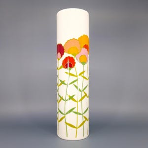 May include: A white, cylindrical vase featuring a floral pattern. The flowers are in shades of red, orange, and pink, with green stems and leaves. A decorative item for the home.