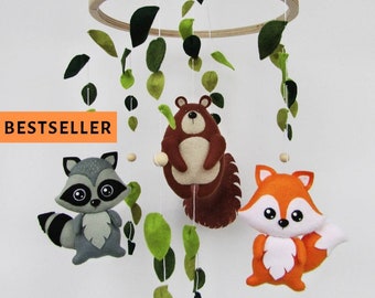May include: A wooden baby mobile with a fox, raccoon, and bear hanging from it. The mobile is decorated with green felt leaves.