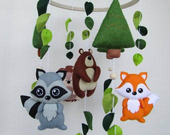 May include: A wooden baby mobile with a green felt tree, a brown bear, a raccoon, a fox, and green felt leaves hanging from a wooden ring.