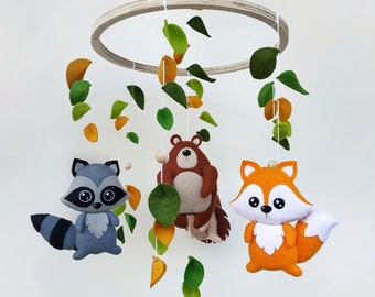 May include: A wooden baby mobile with felt woodland animals, including a raccoon, fox, and bear. The mobile also features green and orange felt leaves.