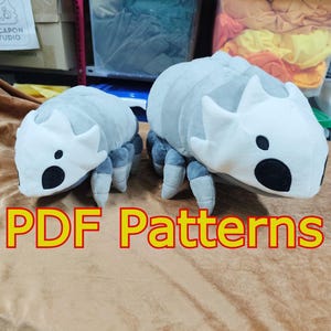 Könnte beinhalten: Zwei Plüschtiere in Form stilisierter Insekten. Die Spielzeuge sind hauptsächlich grau und weiß, mit schwarzen kreisförmigen Details. Der Text "PDF Patterns" wird in großen, orangefarbenen Buchstaben am unteren Bildrand angezeigt.