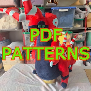Può includere: Un peluche a forma di creatura con corpo rosso e blu scuro, dotato di corna e dettagli a righe azzurre. Il giocattolo presenta un petto blu scuro, arti rossi e una testa stilizzata. Il testo PDF PATTERNS è sovrapposto all'immagine.