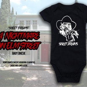 May include: Black baby onesie featuring a white graphic of Freddy Krueger with the text "SWEET DREAMS". The text "A NIGHTMARE ON ELM STREET" is also displayed. The onesie is designed for newborns to 24 months and is available in short and long sleeve.