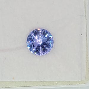 May include: A round, faceted, light blue gemstone with a purple hue.