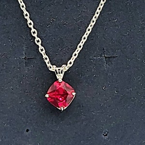 May include: A gold chain necklace with a red gemstone pendant. The gemstone is a square shape with rounded corners.