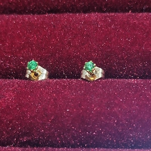 May include: A pair of gold earrings with small green gemstones.