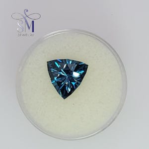 May include: A triangular blue gemstone with a faceted cut, set against a white background.