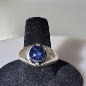 May include: A silver ring with a blue star sapphire gemstone. The gemstone has a star-like pattern.