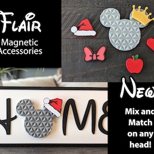 May include: A white sign with the word "HOME" in black letters. A gray Mickey Mouse head with a red Santa hat is in the middle of the sign. The sign is surrounded by a black frame. The image also shows a variety of magnetic accessories, including a red apple, a red heart, a red bow, a gold crown, and a red Santa hat.