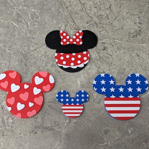 Könnte beinhalten: Drei Filz-Ausschnitte von Mickey Mouse Köpfen. Einer ist rot mit weißen Punkten, einer ist rot mit weißen Herzen und einer ist blau mit weißen Sternen und roten und weißen Streifen.