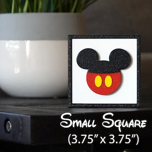 May include: A black framed square wall art piece with a white background featuring a red and black Mickey Mouse head with yellow circles for eyes. The text "Small Square (3.75" x 3.75")" is printed below the image.