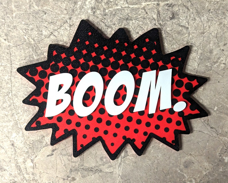 Peut inclure: Une bulle de dialogue de style bande dessin&eacute;e rouge et noire avec le mot "BOOM!" en lettres blanches.