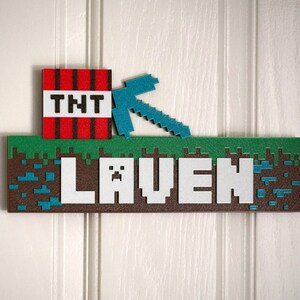 May include: A Minecraft-themed name sign with the name "Laven" in white letters on a brown background. The sign features a green grass block, a blue pickaxe, and a red TNT block.
