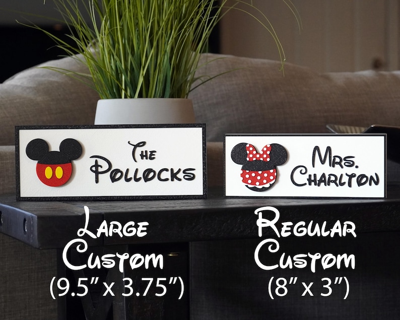 May include: Two custom wooden signs with Mickey Mouse and Minnie Mouse characters. The larger sign is 9.5 inches by 3.75 inches and reads "The Pollocks". The smaller sign is 8 inches by 3 inches and reads "Mrs. Charlton".