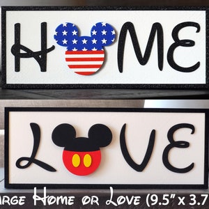 May include: Two wooden signs with black frames and white backgrounds. The top sign says "HOME" with a red, white, and blue Mickey Mouse head in the middle. The bottom sign says "LOVE" with a black Mickey Mouse head with red ears and yellow circles for eyes.