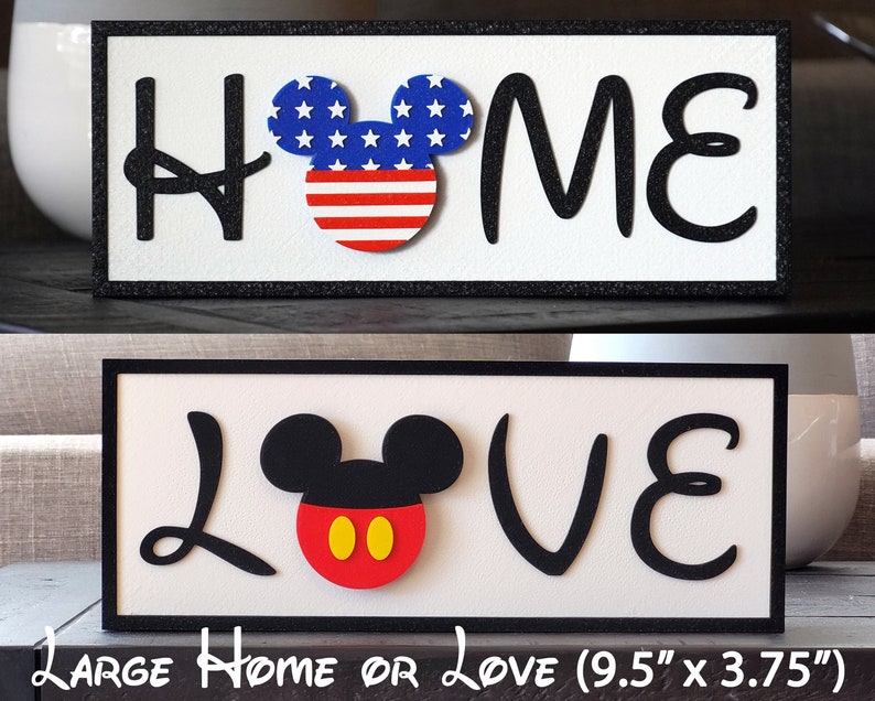 May include: Two wooden signs with black frames and white backgrounds. The top sign says "HOME" with a red, white, and blue Mickey Mouse head in the middle. The bottom sign says "LOVE" with a black Mickey Mouse head with red ears and yellow circles for eyes.