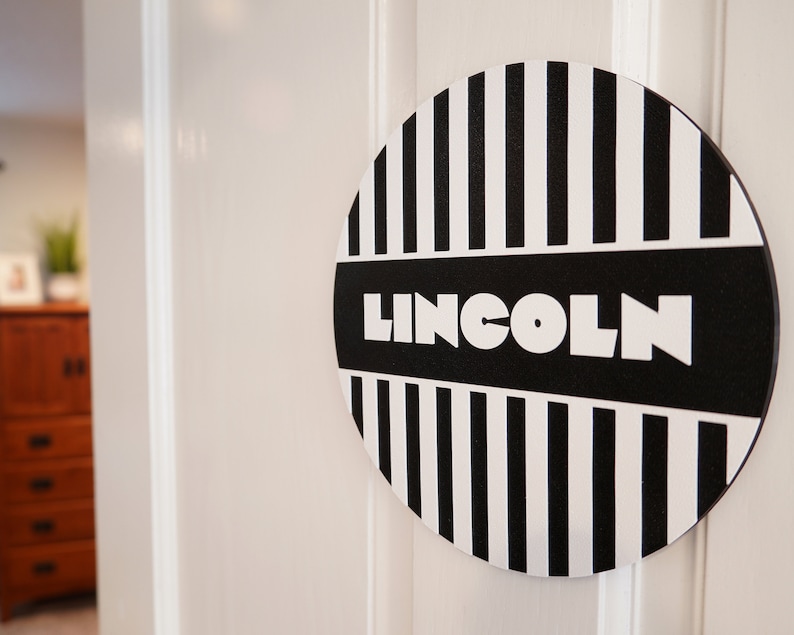 May include: A black and white striped round sign with the word "LINCOLN" in white letters on a black background.