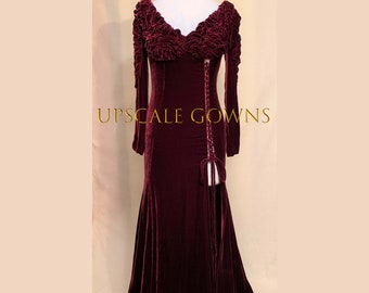 May include: A long-sleeved, burgundy velvet gown with a ruffled neckline and a lace-up detail on the side. The gown has a fitted bodice and a flowing skirt with a high slit.