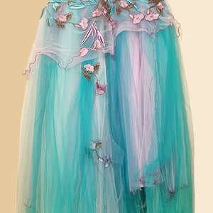 May include: A long, flowing tulle gown with a gradient of turquoise and pink. The gown features delicate floral embroidery and a ruffled hem.