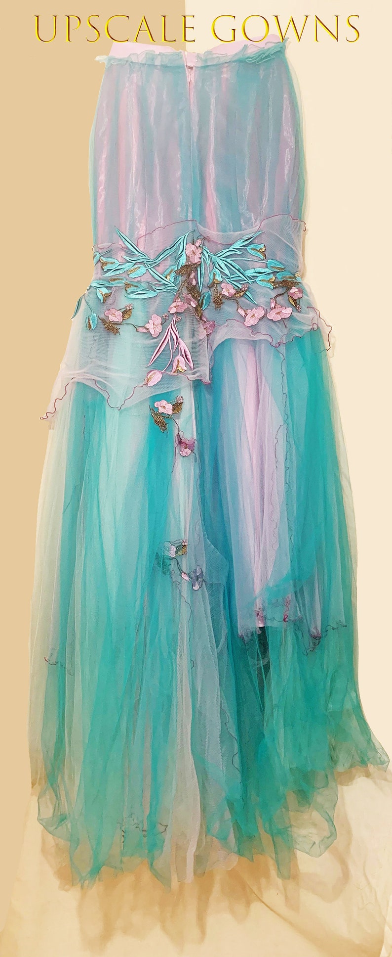 May include: A long, flowing tulle gown with a gradient of turquoise and pink. The gown features delicate floral embroidery and a ruffled hem.