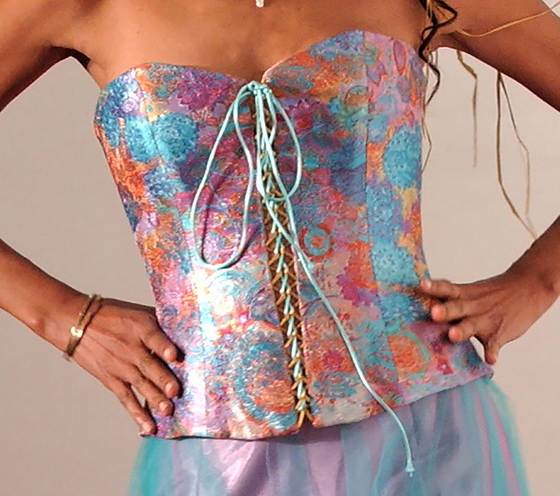 May include: A strapless corset with a colorful floral pattern and a turquoise lace-up front. The corset is made of a silky fabric and has a fitted silhouette.
