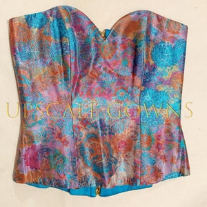 May include: A strapless corset with a vibrant floral print in shades of pink, blue, and orange. The fabric has a metallic sheen and a textured pattern.